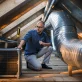 hvac technician inspecting air conditioner unit and ductwork in attic photo